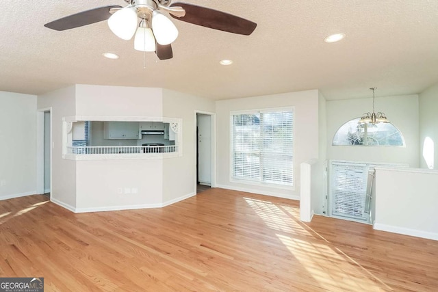 unfurnished living room with hardwood / wood-style floors, ceiling fan with notable chandelier, and a textured ceiling