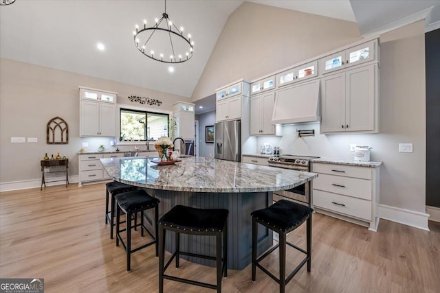 kitchen featuring appliances with stainless steel finishes, light stone counters, custom exhaust hood, a center island with sink, and white cabinets