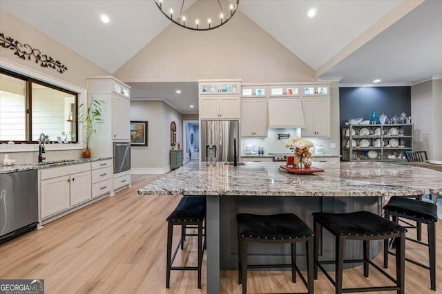 kitchen featuring light stone countertops, stainless steel appliances, a spacious island, sink, and white cabinets