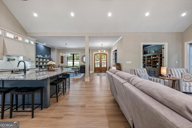 living room featuring sink, vaulted ceiling, light hardwood / wood-style flooring, ornamental molding, and a chandelier