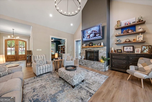 living room featuring a fireplace, french doors, light wood-type flooring, and a notable chandelier