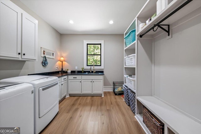 laundry room featuring washing machine and clothes dryer, sink, cabinets, and light hardwood / wood-style flooring