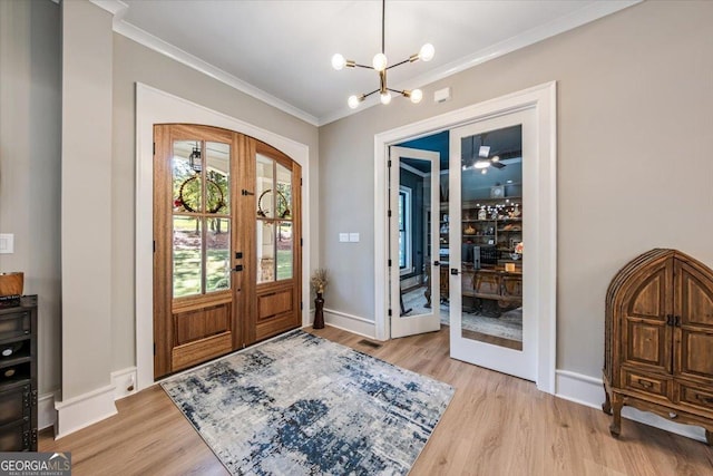 foyer featuring crown molding, french doors, light wood-type flooring, and an inviting chandelier