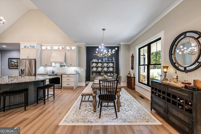 dining space featuring a notable chandelier, light hardwood / wood-style floors, ornamental molding, and vaulted ceiling