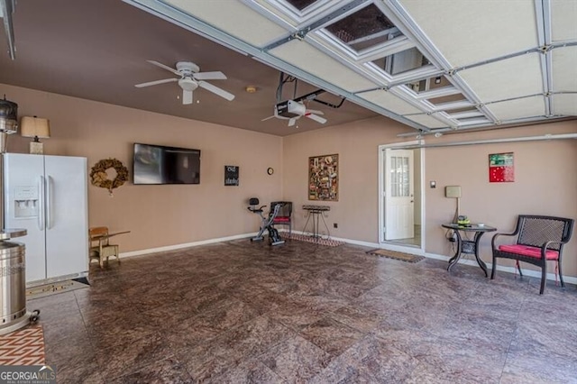 garage featuring ceiling fan, baseboards, a garage door opener, and white fridge with ice dispenser
