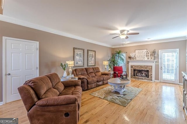 living room with light wood-type flooring, a fireplace, ceiling fan, and crown molding