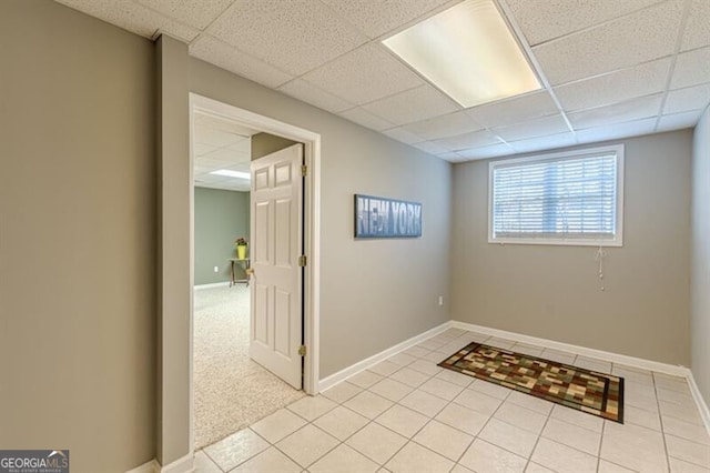 interior space with a paneled ceiling, baseboards, and light tile patterned flooring