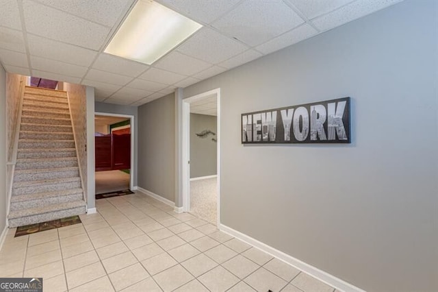 finished below grade area featuring baseboards, stairs, a drop ceiling, and light tile patterned floors