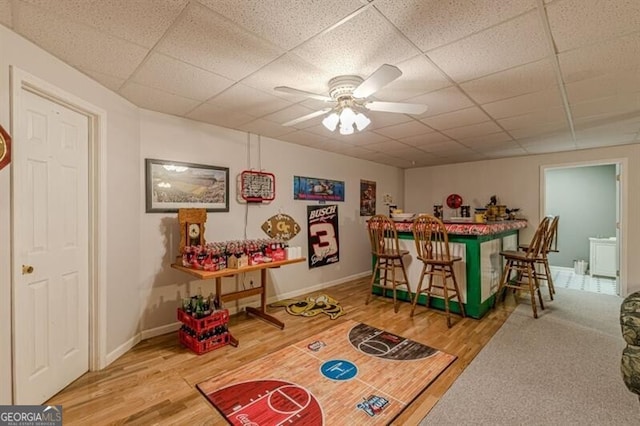 playroom with ceiling fan, wood finished floors, a bar, and a drop ceiling