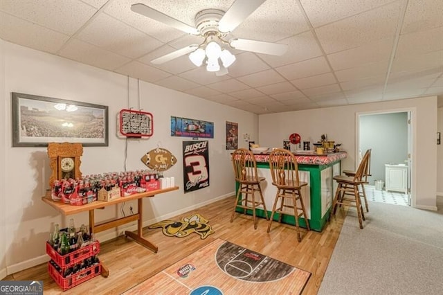 game room with ceiling fan, baseboards, a bar, and a drop ceiling