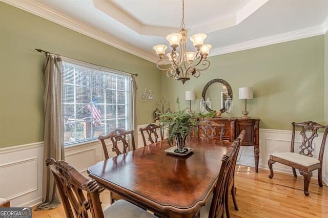 dining space featuring light wood finished floors, a wainscoted wall, a tray ceiling, a notable chandelier, and a decorative wall