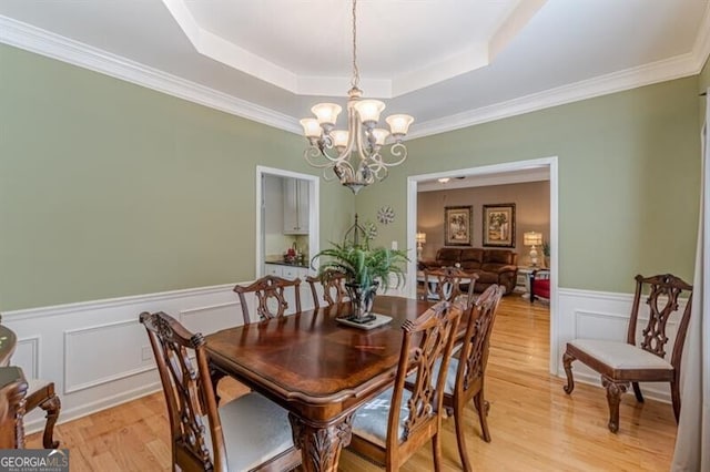 dining room with a tray ceiling, ornamental molding, light wood-style floors, wainscoting, and a chandelier