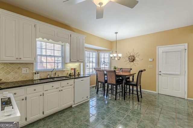 kitchen featuring dark countertops, white dishwasher, a sink, and tasteful backsplash
