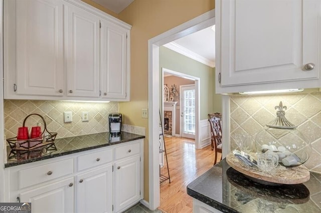 kitchen featuring dark stone countertops, decorative backsplash, light wood finished floors, white cabinetry, and ornamental molding
