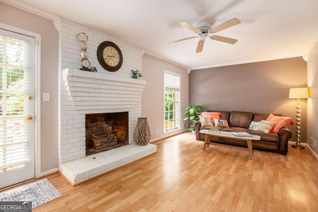 living room with crown molding, ceiling fan, light wood-type flooring, and a brick fireplace