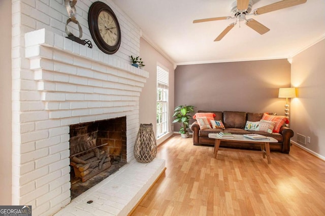 living room featuring crown molding, a fireplace, ceiling fan, and light hardwood / wood-style flooring