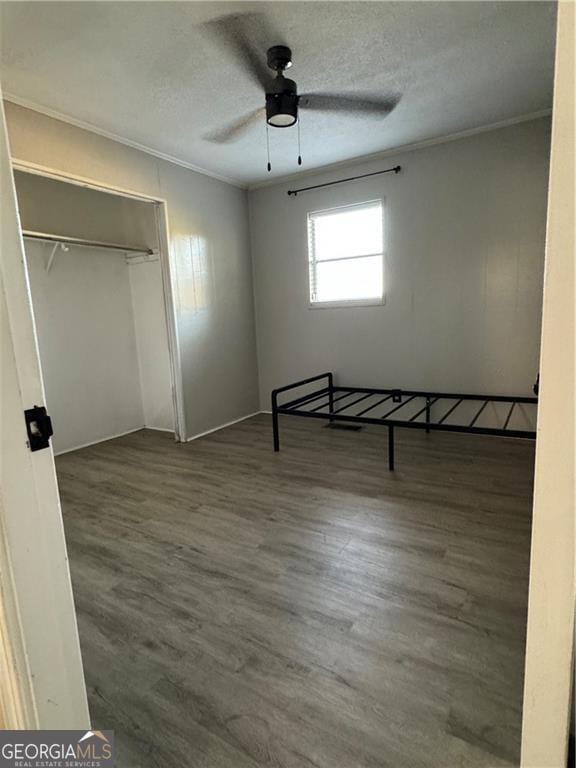 unfurnished bedroom with ornamental molding, a closet, dark wood-type flooring, and ceiling fan