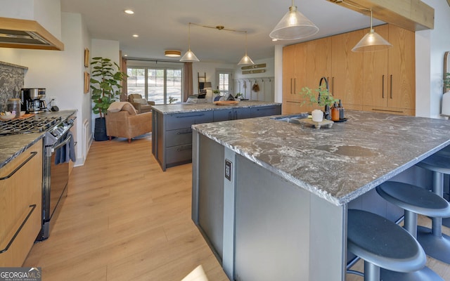 kitchen with stainless steel gas range oven, dark stone counters, extractor fan, decorative light fixtures, and a center island