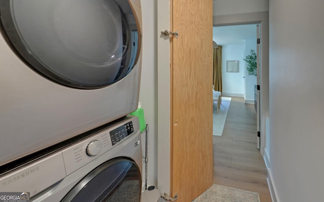 laundry area with baseboards, stacked washer and dryer, laundry area, and light wood-style floors
