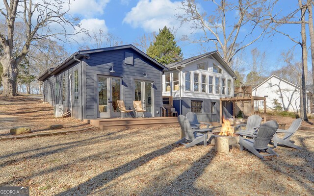 rear view of property with a sunroom, a deck, and an outdoor fire pit