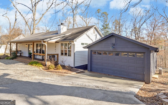 ranch-style home with a porch, a chimney, aphalt driveway, and an outbuilding