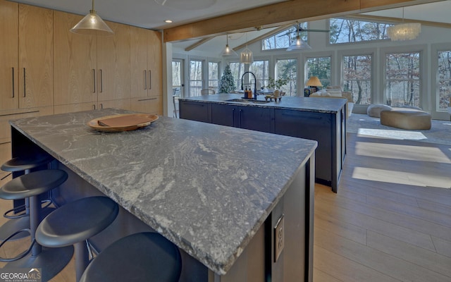 kitchen with lofted ceiling with beams, a sink, modern cabinets, light brown cabinets, and an island with sink