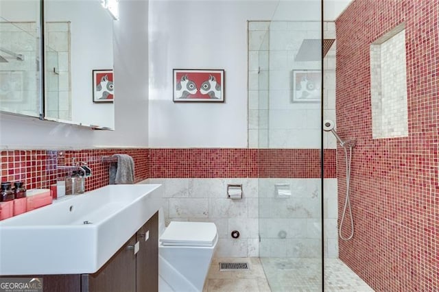 bathroom featuring backsplash, toilet, tiled shower, vanity, and tile walls