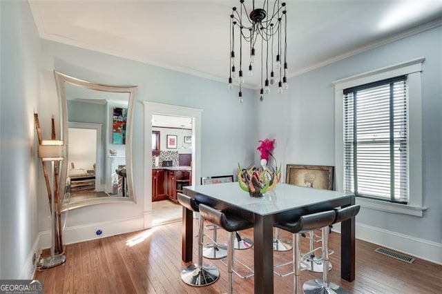 dining space featuring crown molding, plenty of natural light, wood-type flooring, and an inviting chandelier