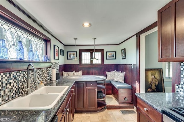 kitchen with dark stone counters, sink, pendant lighting, and ornamental molding