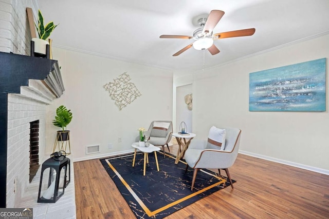 sitting room with ceiling fan, wood-type flooring, ornamental molding, and a brick fireplace