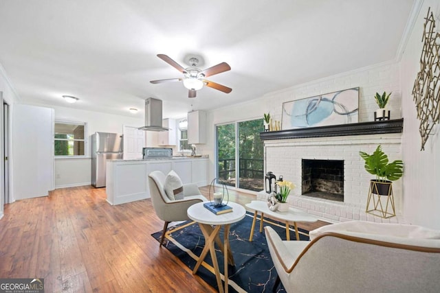 living room featuring a fireplace, light wood-type flooring, ceiling fan, and a healthy amount of sunlight