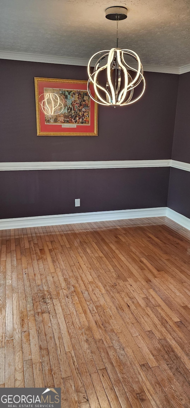 unfurnished dining area featuring hardwood / wood-style flooring, crown molding, a textured ceiling, and a chandelier