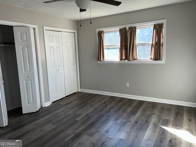 unfurnished bedroom featuring ceiling fan, dark wood-type flooring, and two closets