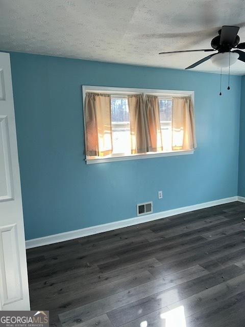 spare room with a textured ceiling, ceiling fan, and dark hardwood / wood-style floors