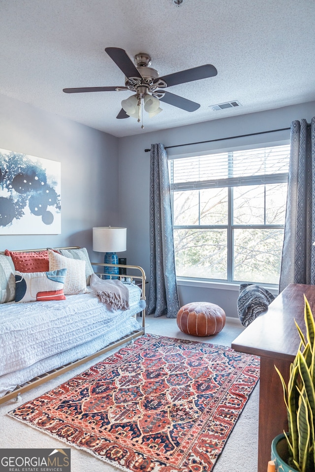 carpeted bedroom with ceiling fan and a textured ceiling