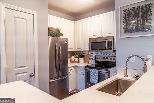 kitchen with light stone countertops, sink, stainless steel appliances, decorative backsplash, and white cabinets