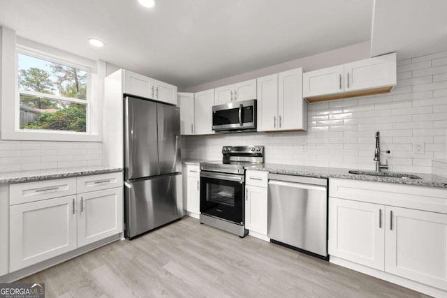 kitchen with sink, stainless steel appliances, tasteful backsplash, light stone counters, and white cabinets