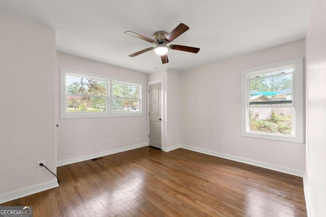 empty room featuring a wealth of natural light, dark wood-type flooring, and ceiling fan