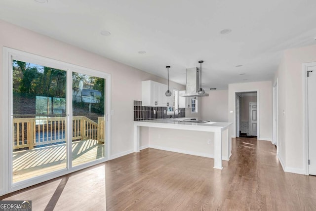 kitchen featuring hanging light fixtures, kitchen peninsula, island range hood, a breakfast bar, and white cabinets