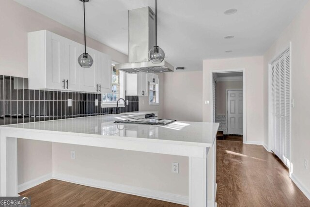 kitchen featuring kitchen peninsula, island range hood, dark wood-type flooring, decorative light fixtures, and white cabinets