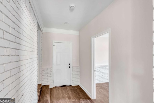 hall with hardwood / wood-style flooring, ornamental molding, and brick wall