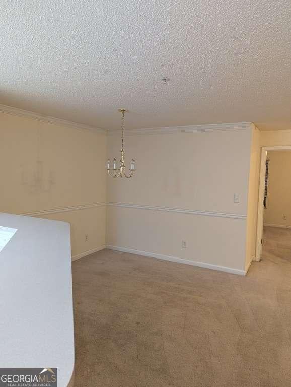 carpeted spare room featuring a chandelier, a textured ceiling, and crown molding