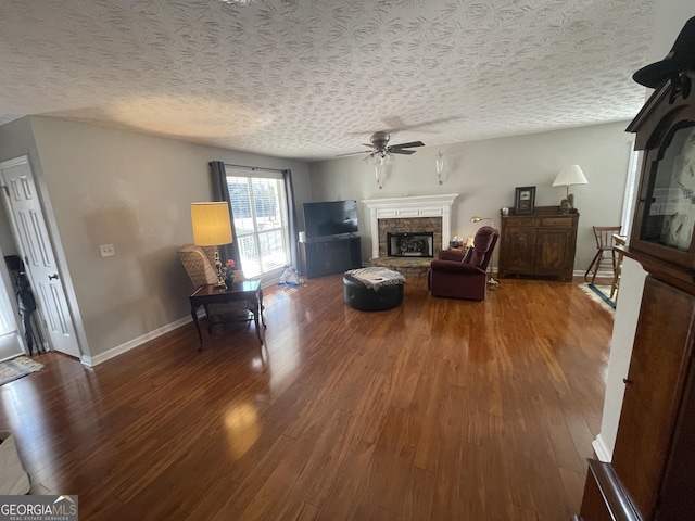 living room featuring wood-type flooring, a textured ceiling, a stone fireplace, and ceiling fan