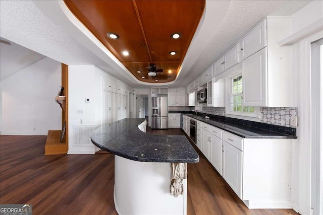 kitchen featuring appliances with stainless steel finishes, white cabinetry, a kitchen island, dark hardwood / wood-style flooring, and a raised ceiling