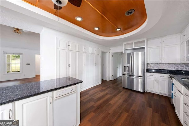 kitchen featuring dark stone countertops, stainless steel appliances, a tray ceiling, white cabinets, and dark hardwood / wood-style flooring