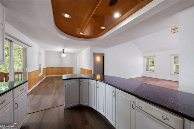 kitchen featuring dark wood-type flooring, white cabinetry, dark stone countertops, white dishwasher, and a raised ceiling