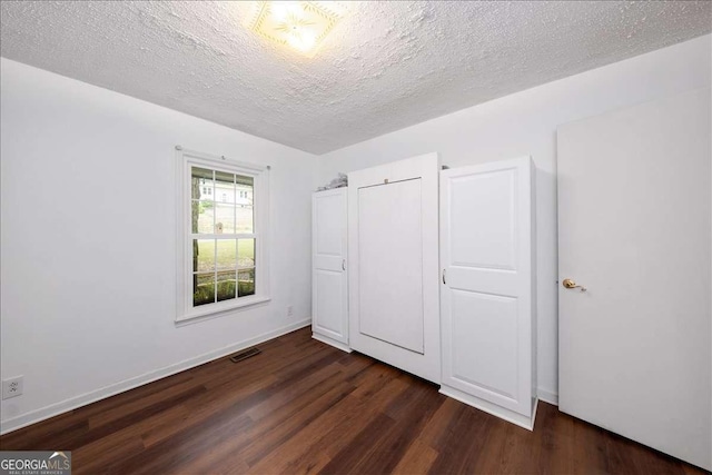 unfurnished bedroom with dark wood-type flooring, a textured ceiling, and a closet