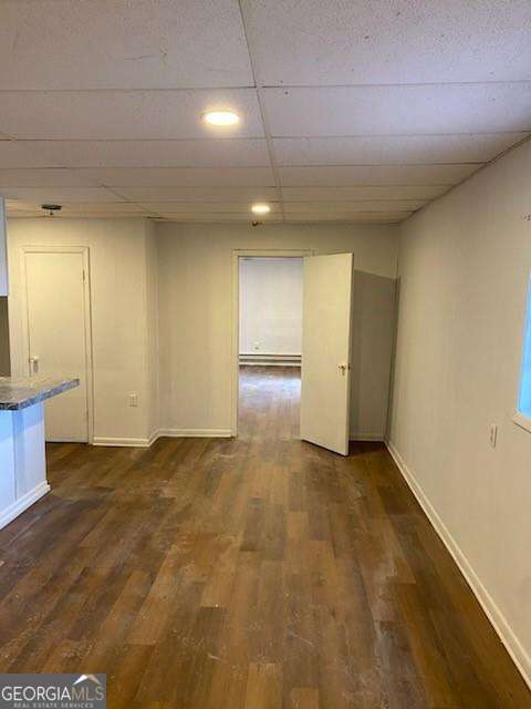 empty room with dark hardwood / wood-style flooring and a drop ceiling