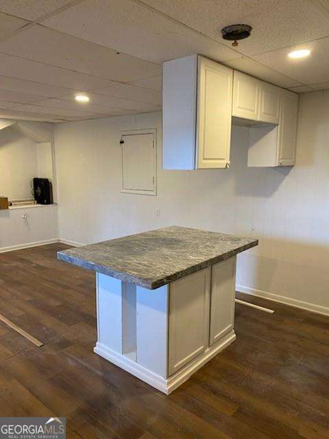 kitchen with a paneled ceiling, dark wood-type flooring, dark stone countertops, and white cabinets