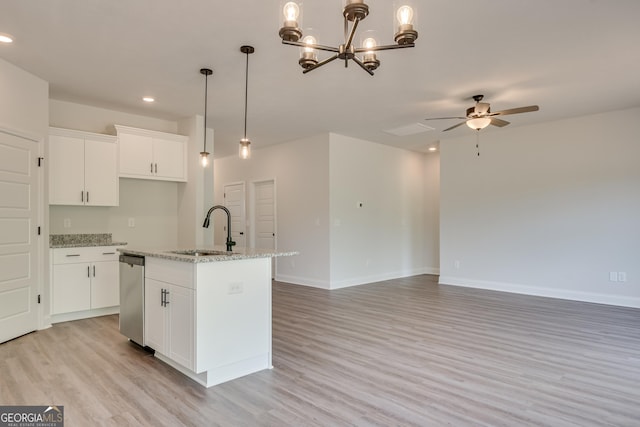 kitchen with pendant lighting, sink, light stone countertops, an island with sink, and white cabinetry